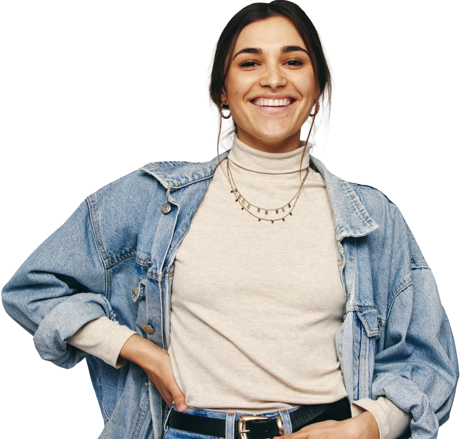 Smiling young woman with dark hair wearing a light denim jacket over a cream turtleneck, standing with hands on hips